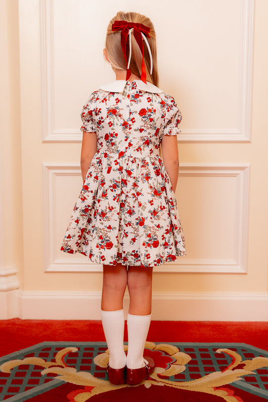 the back of a little girl in a white floral dress standing against a white wall