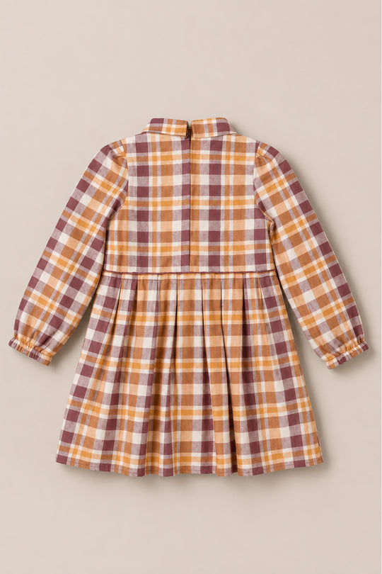 A back view of the Ivy City Co Mini Bowie Long Sleeve Dress in Spiced Plaid for kids, featuring a knee-length, long-sleeved design with a brown, yellow, and white plaid pattern. This girls’ cotton dress includes a gathered skirt and elastic cuffs for added comfort.