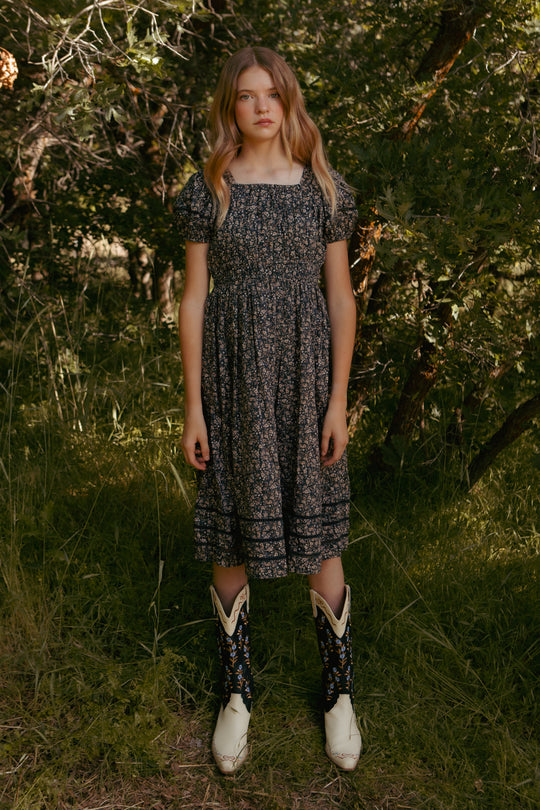 teenager in a floral dress and boots standing in a forest