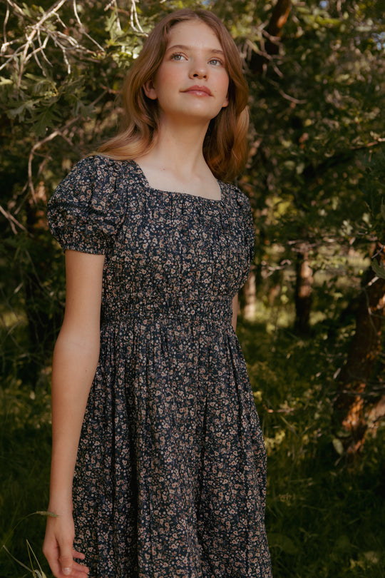teenager wearing a floral dress standing in a forest