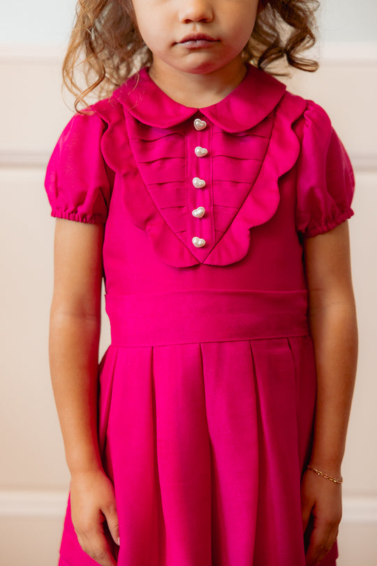 close up of a little girl in a pink dress standing against a white wall
