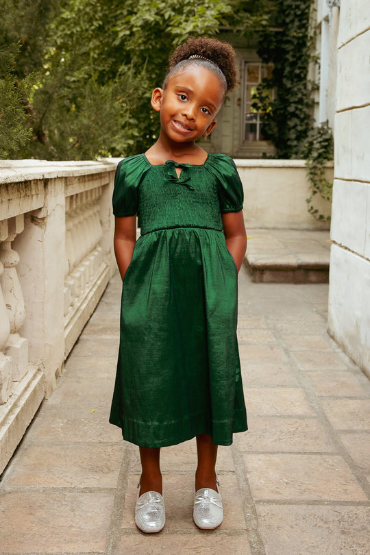 Young girl in a green dress standing on a stone path with greenery in the background