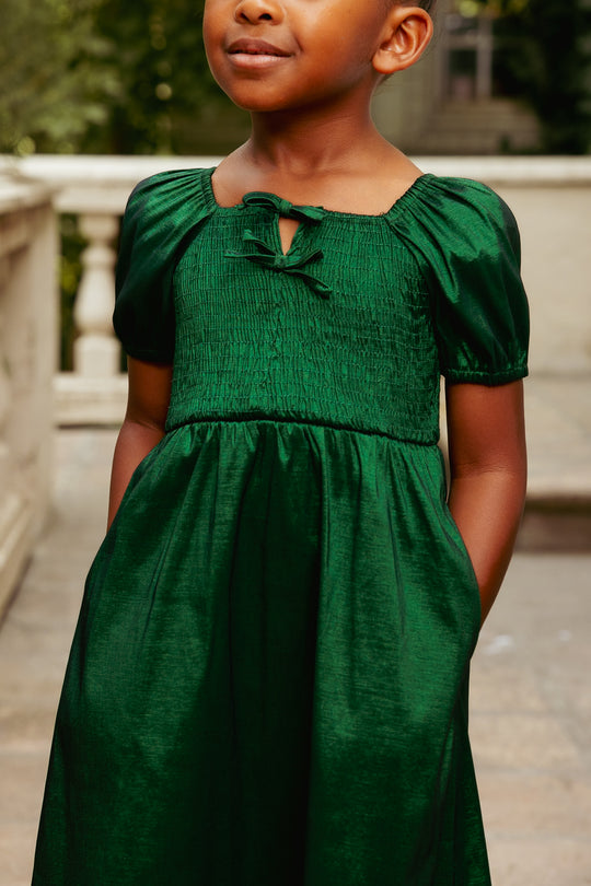 Young girl wearing a green dress standing outdoors.
