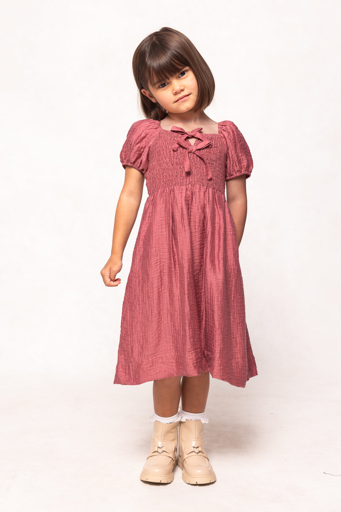 Young girl wearing a pink dress with puff sleeves on a white background
