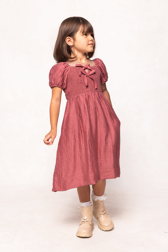 Young girl wearing a pink dress with puff sleeves on a white background