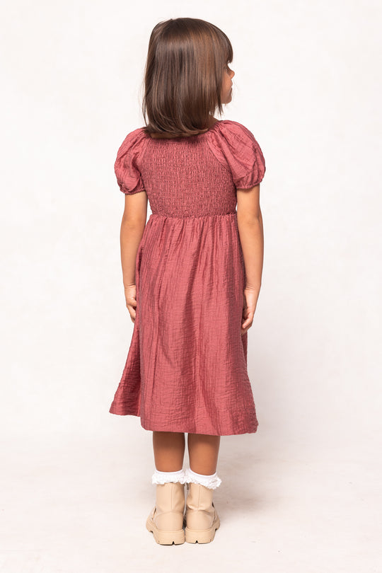 Young girl wearing a pink dress with puffed sleeves on a white background