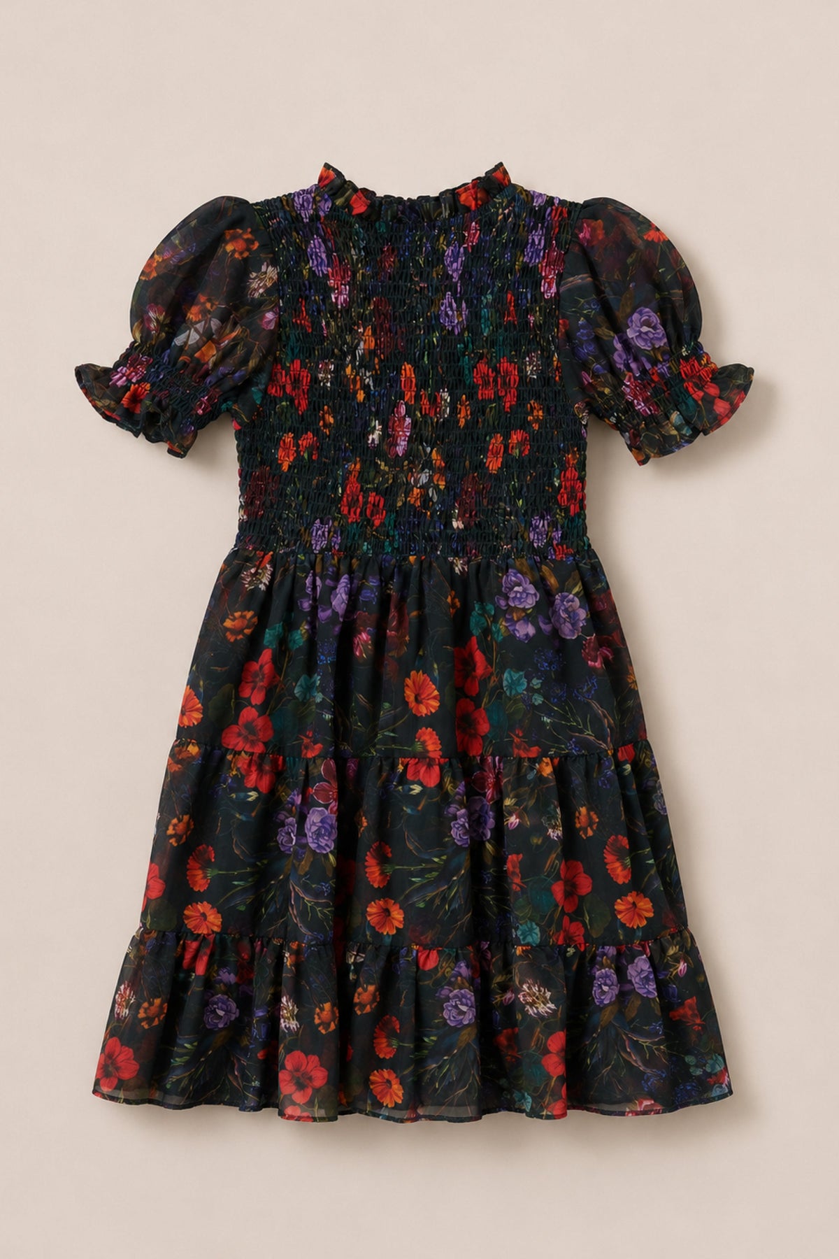 The Ivy City Co Mini Cordelia Dress in Evergreen Vivid Meadow features a smocked bodice and charming puff sleeves, designed in a short-sleeve, knee-length silhouette with a vibrant floral print of red, purple, and green on a classic black background.