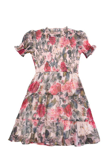 The Ivy City Co Mini Cordelia Dress in Pink Bloom is a girls’ knee-length chiffon dress with ruffled short sleeves, a smocked bodice, and a pink, red, and green floral pattern for a layered, flared look.