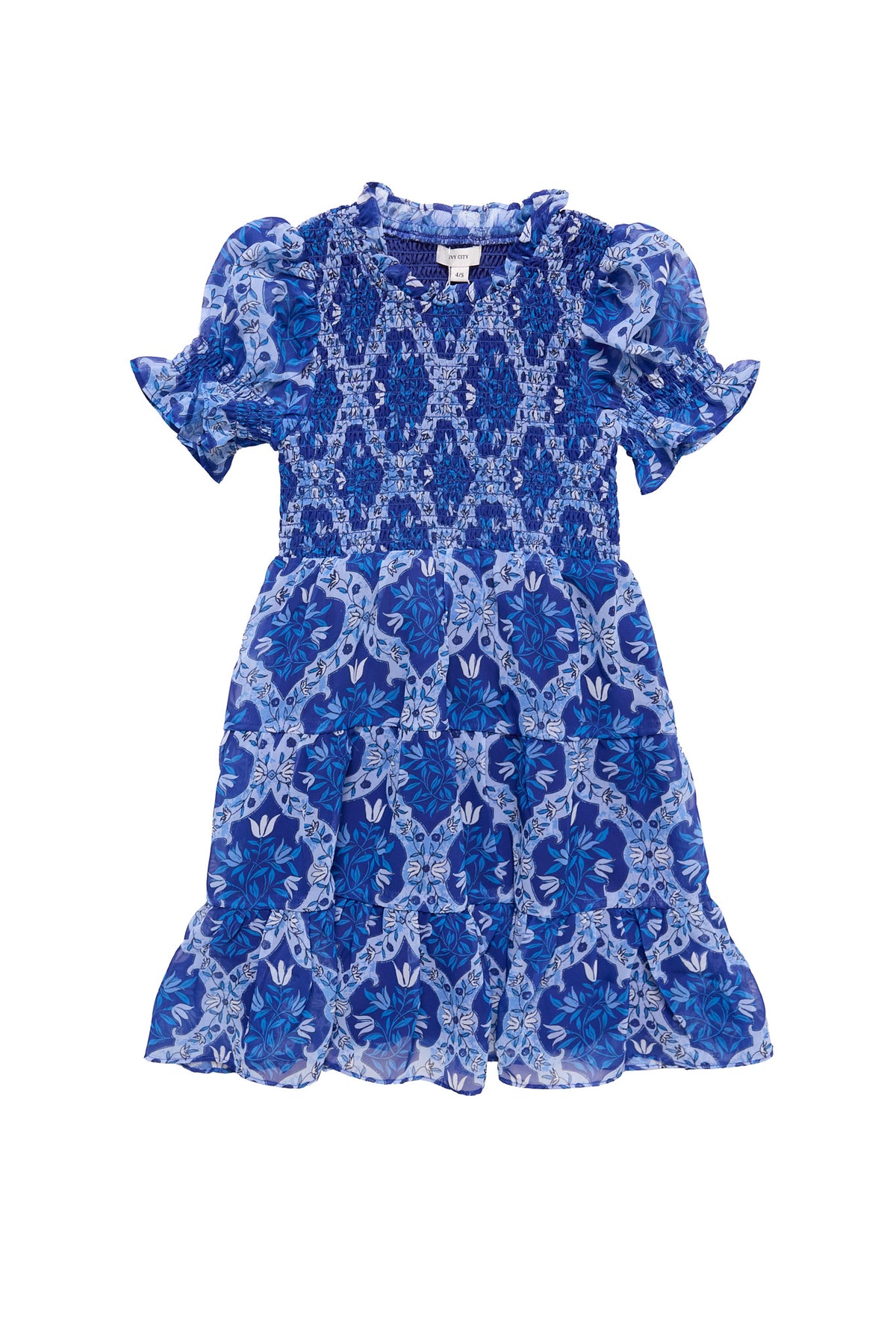 The Ivy City Co Mini Cordelia Dress in Trellis Foulard features blue and white floral and geometric patterns, puffed sleeves, a smocked bodice, and a ruffled hem—ideal for matching family looks. Laid flat on a white background.