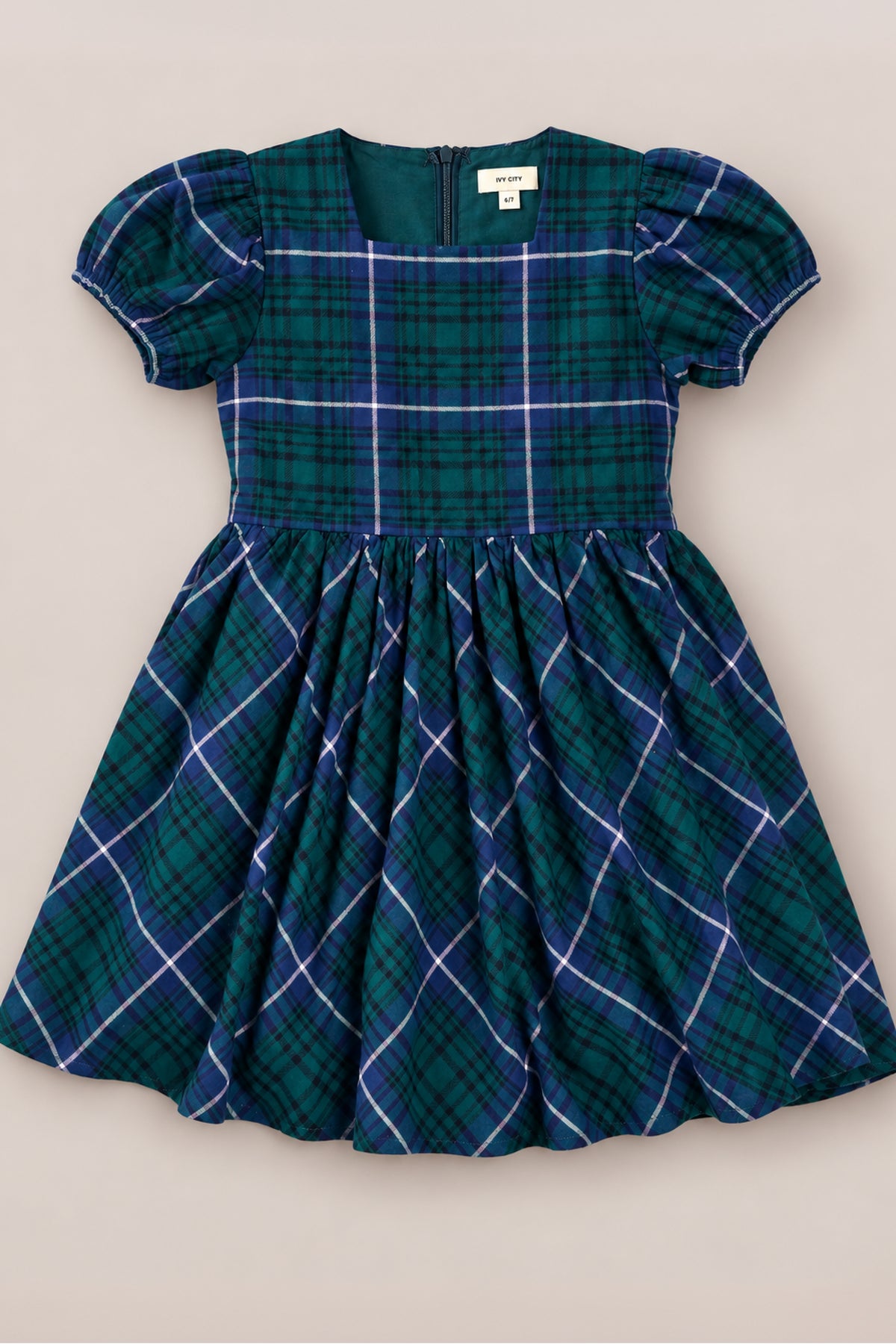 The Mini Cupcake Dress in Emerald Plaid by Ivy City Co features green and blue plaid, puffed short sleeves, a fitted bodice, gathered skirt, and a back zipper—making it the perfect holiday dress for girls to wear at festive gatherings or family photos. Shown on a plain background.