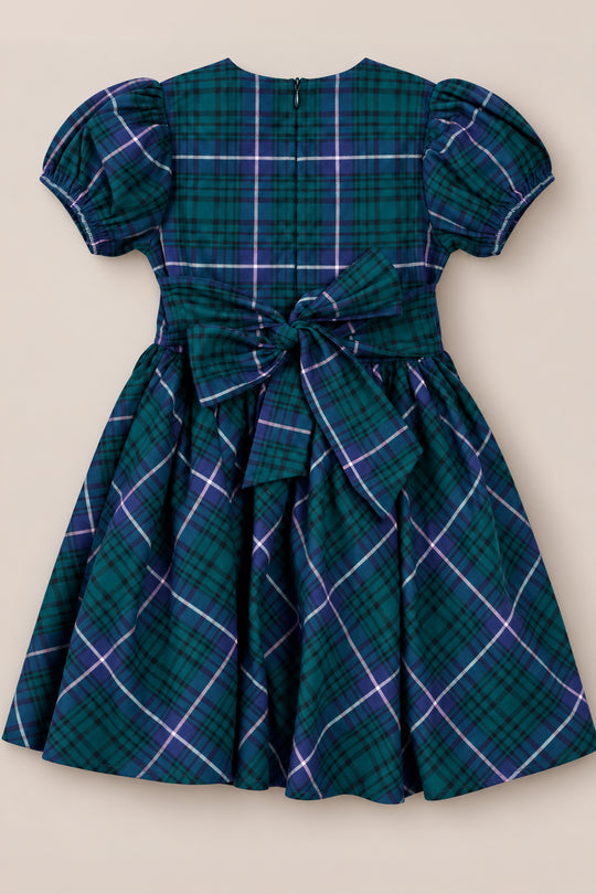 The Ivy City Co Mini Cupcake Dress in Emerald Plaid features a charming blue and green plaid pattern, puff sleeves, and a large bow tied at the back—making it the perfect choice for festive gatherings or as a standout family photo dress.