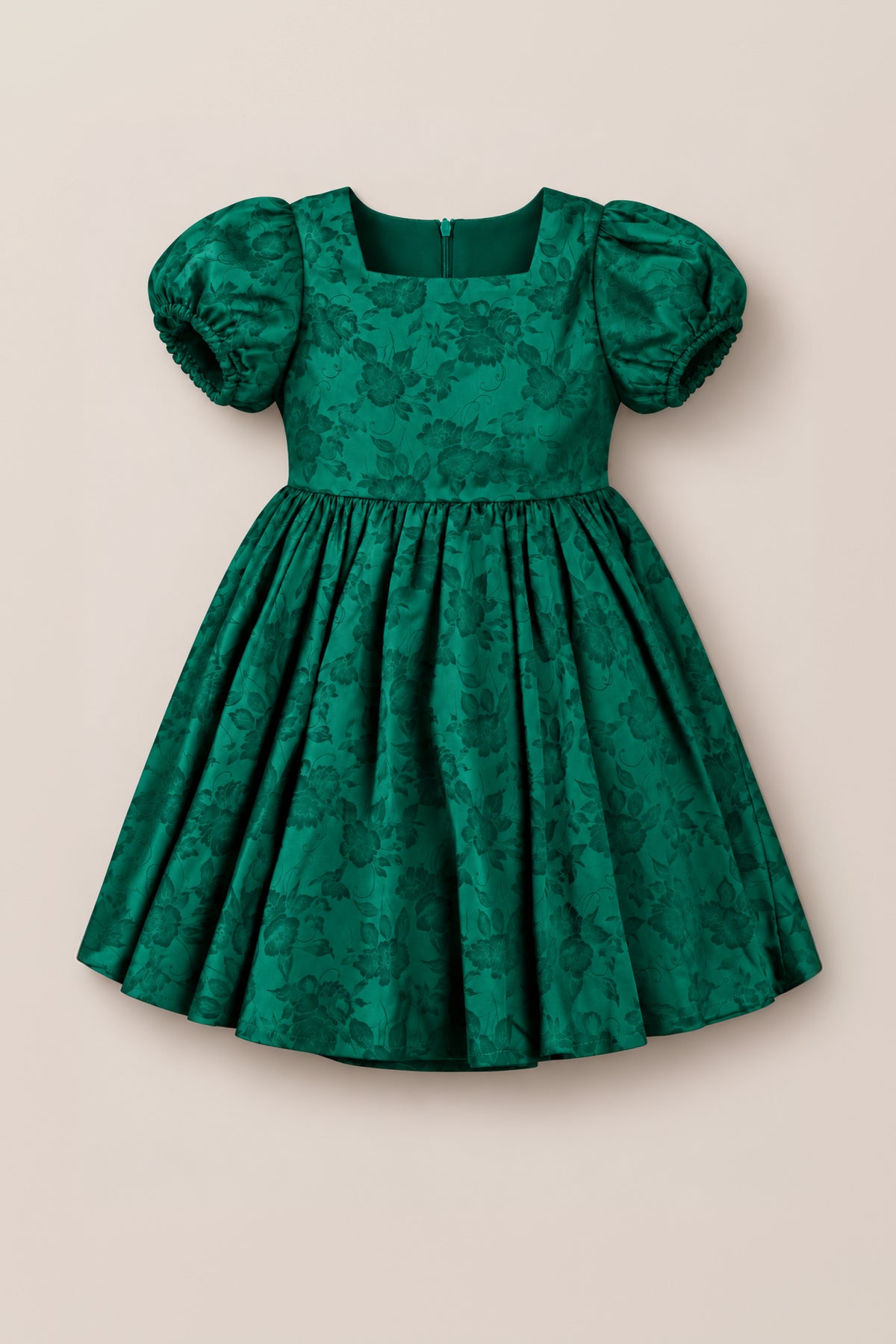 Make her holiday shine with the Mini Cupcake Dress in Emerald Satin by Ivy City Co, featuring a fitted bodice, puffed short sleeves, and a full skirt. The luxurious satin fabric is adorned with a subtle floral pattern for festive charm, complete with a back zipper closure. This girls’ festive dress is shown against a plain light beige background.