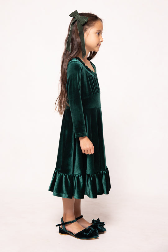 Young girl wearing a green velvet dress with a bow on a white background