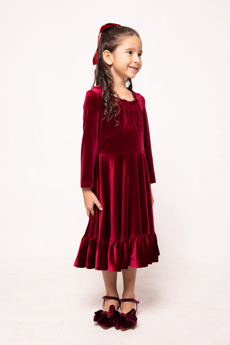 Young girl wearing a red velvet dress with a matching cardigan on a white background