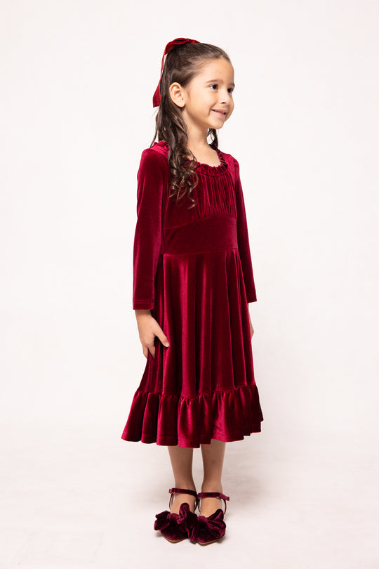 Young girl wearing a red velvet dress with a matching cardigan on a white background