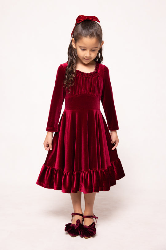 Young girl wearing a red velvet dress with long sleeves and a bow in her hair on a white background