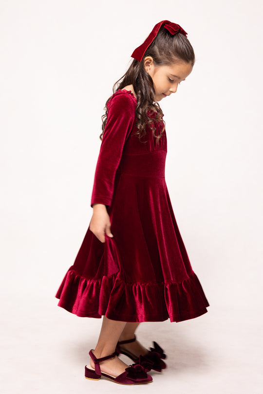 Young girl wearing a red velvet dress with a matching headband on a white background