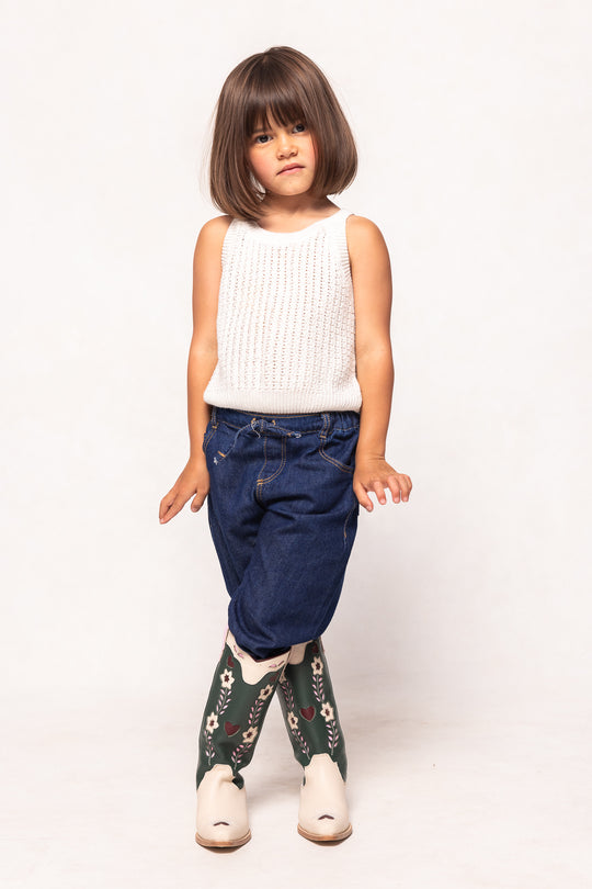 Child wearing a white sleeveless top and blue jeans with floral leggings on a white background