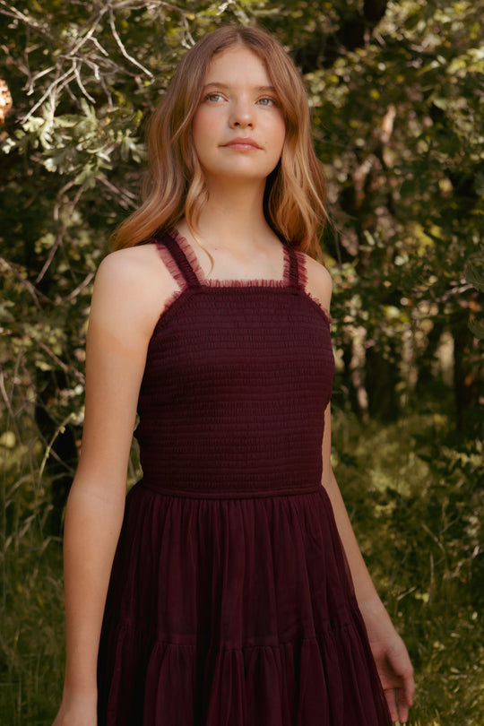Woman wearing a burgundy dress standing in a natural setting with greenery.