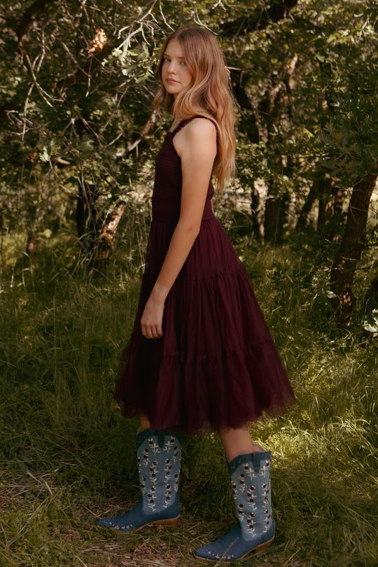 Woman in a burgundy dress and blue boots standing in a forest