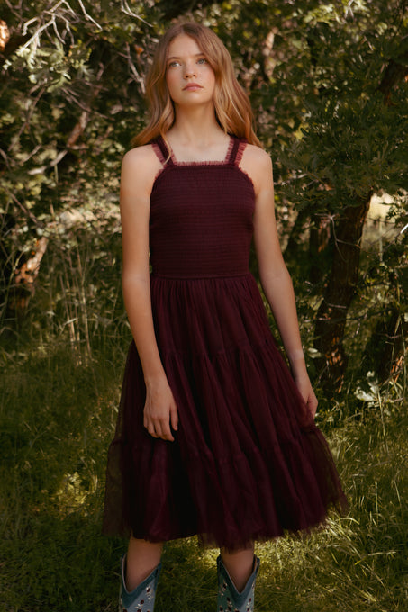 Woman wearing a burgundy dress standing in a natural setting with trees and grass.