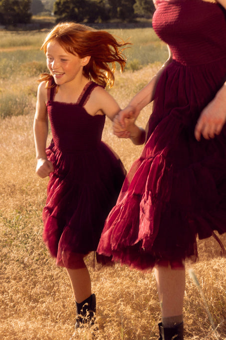 little girl with her mom in red dresses running through a field.