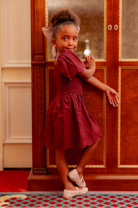 girl in a burgundy dress standing on a red carpet