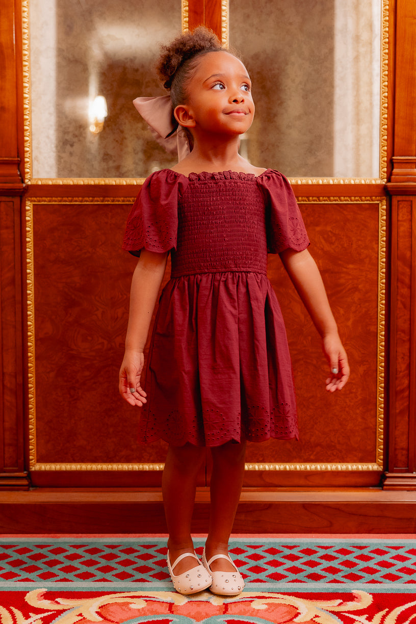 girl in a burgundy dress standing on a red carpet