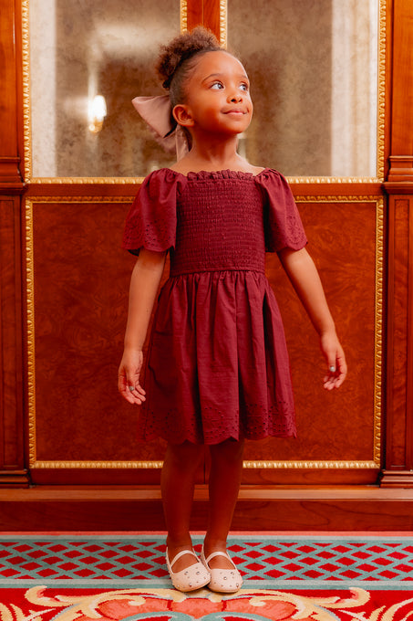 girl in a burgundy dress standing on a red carpet