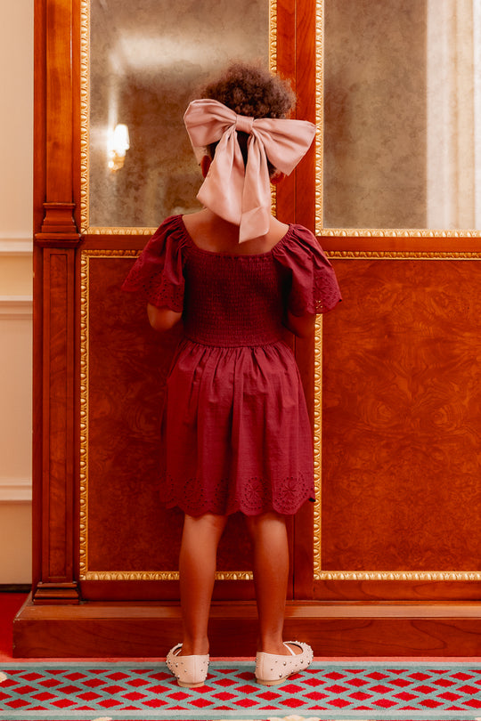 the back of a girl in a burgundy dress standing on a red carpet