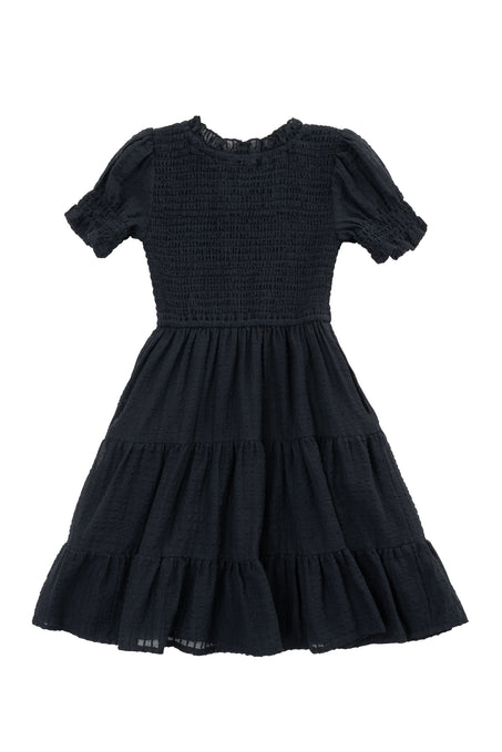 The Ivy City Co Mini Ellery Dress in Black features a smocked bodice, short ruffled sleeves, and a tiered skirt in lightweight textured fabric—perfect for classic matching looks with mom.