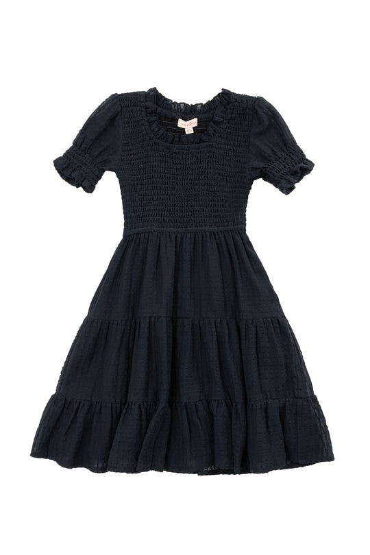 The Mini Ellery Dress in Black by Ivy City Co is a kids’ knee-length, short-sleeved dress with a smocked bodice, ruffled round neckline, tiered skirt, and ruffle trim—ideal for matching mom moments.