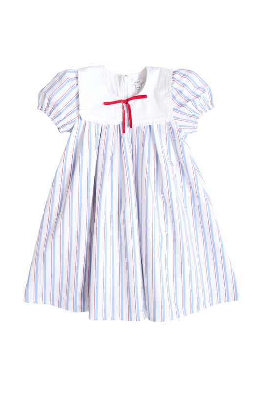 The Mini Emery Dress in Heritage Stripe by Ivy City Co features a white yoke, puffed short sleeves, blue and red vertical stripes, and a red ribbon bow—perfect as a classic red, white, and blue girls’ summer dress for any occasion.