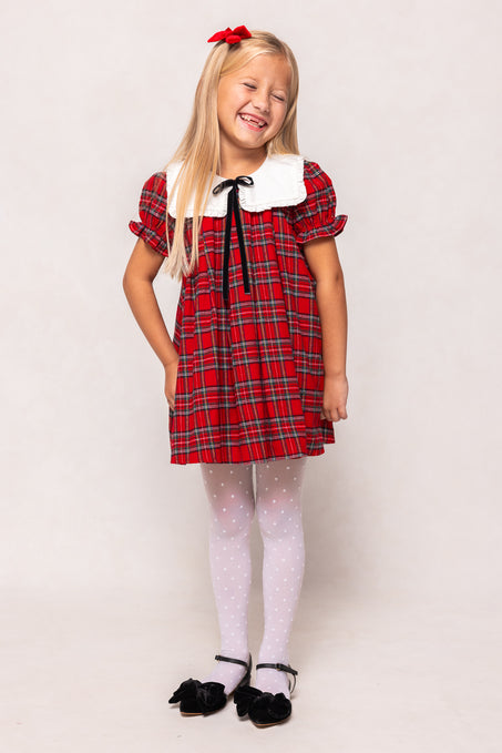 Young girl wearing a red plaid dress with a white collar against a plain background