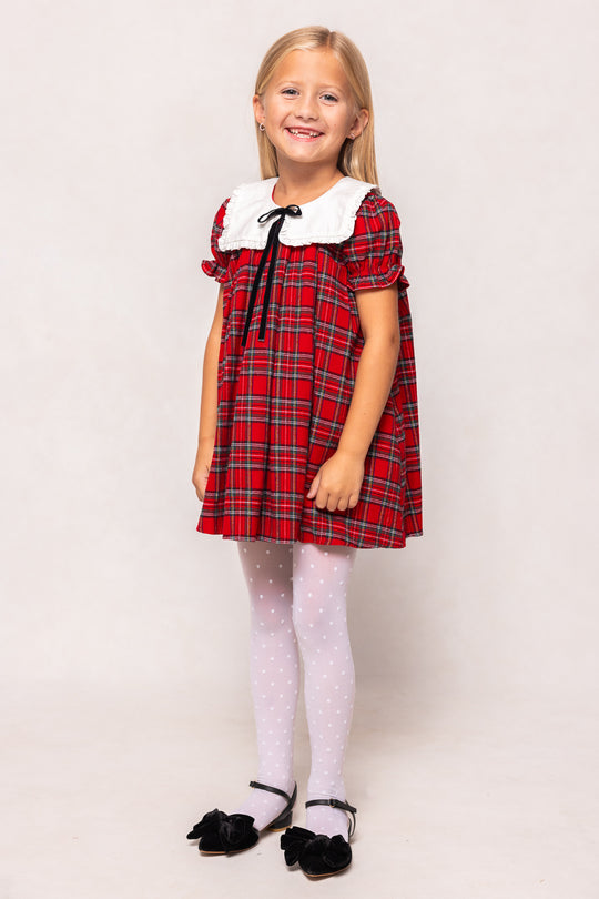 Young girl wearing a red plaid dress with white collar and black shoes on a light background