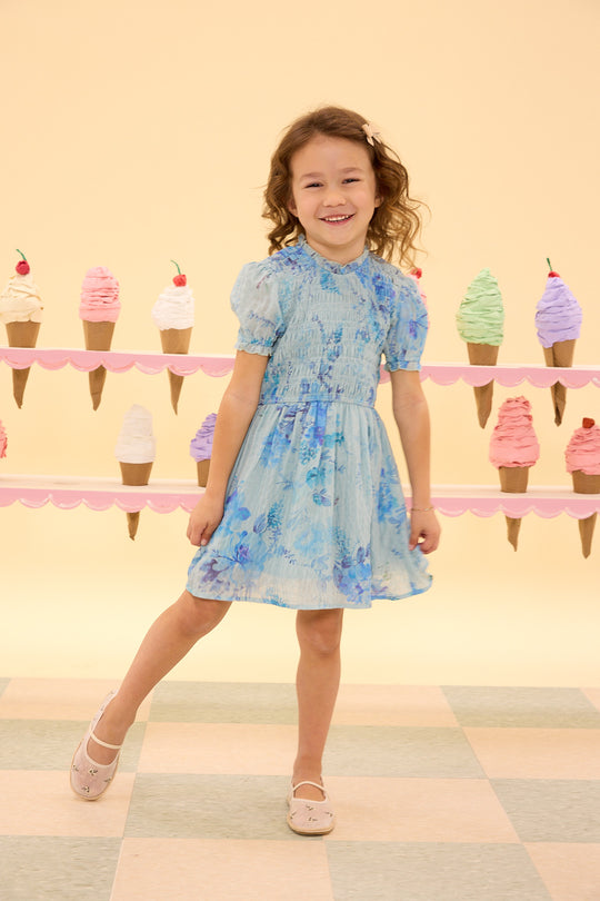 Young girl in a floral dress standing in front of ice cream cone decorations on a checkered floor.