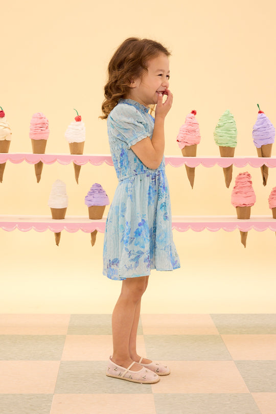 Young girl in a blue floral dress standing in front of ice cream cone decorations on a checkered floor.