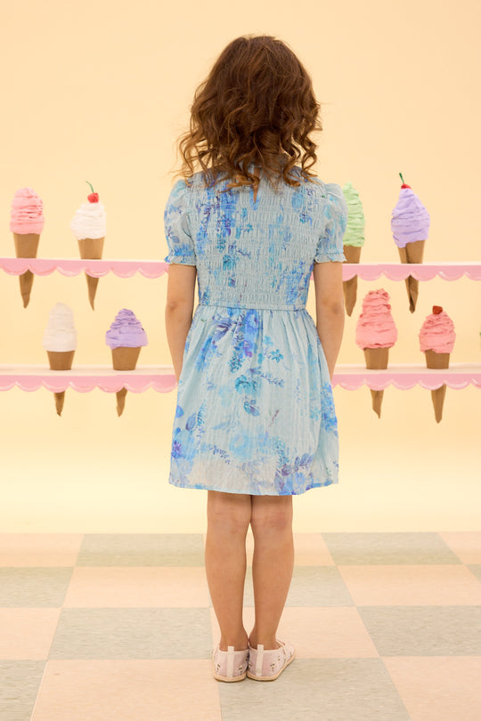 Woman in a floral dress standing in front of ice cream cone decorations on a wall.