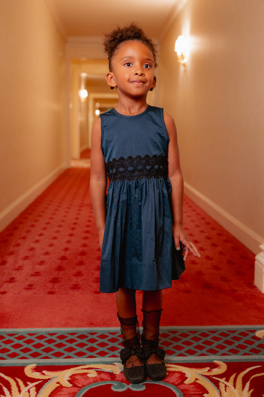Young girl in a blue dress standing on a red carpeted hallway.