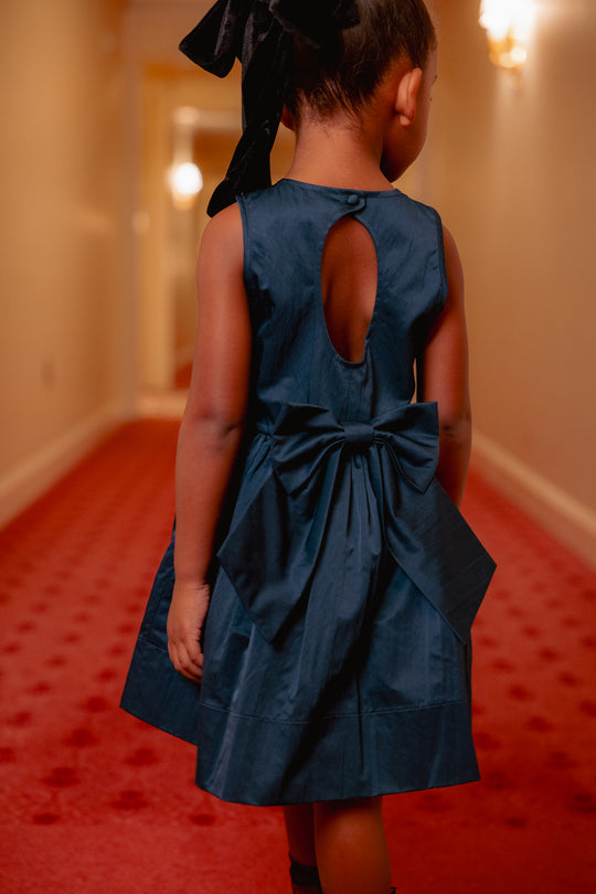 Child wearing a blue dress with a bow in a hallway with red carpet