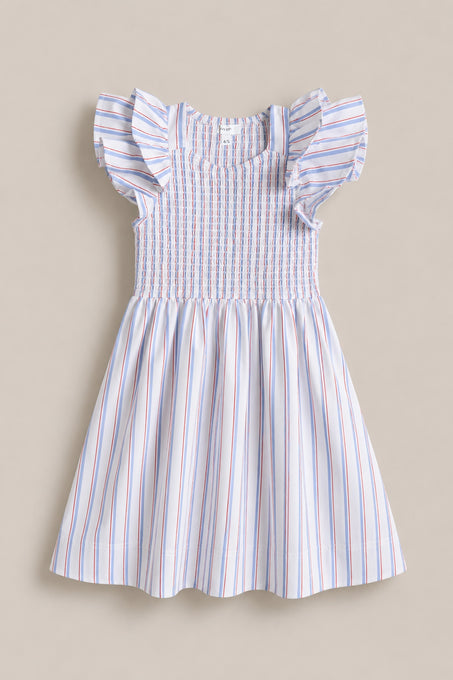The Mini Hattie Dress in Heritage Stripe by Ivy City Co is a sleeveless dress with ruffled shoulders, smocked bodice, and flared skirt in red, blue, and pink stripes—ideal for July 4th or Mom & Me matching. Shown on a neutral surface.