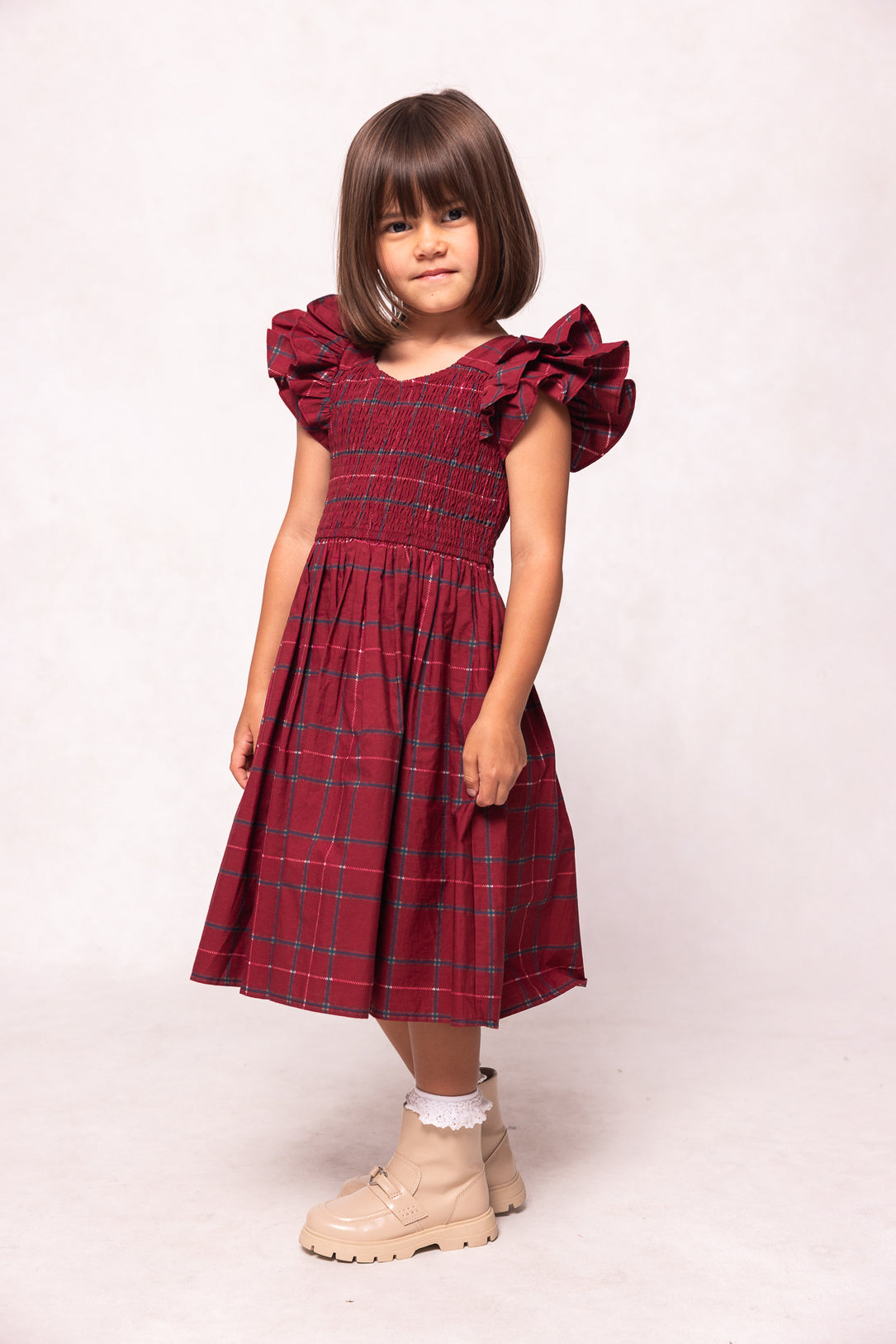 Young girl wearing a red plaid dress with ruffled sleeves on a white background