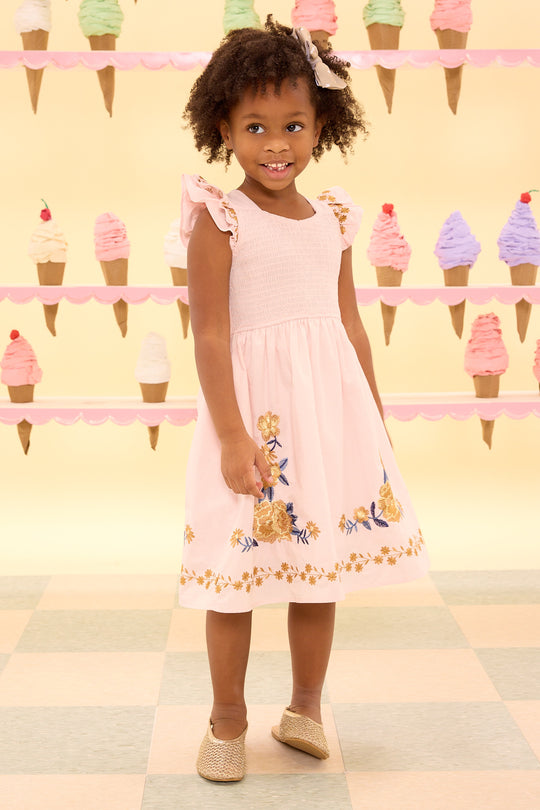 Young girl in a pink dress with floral embroidery standing in front of an ice cream cone display.