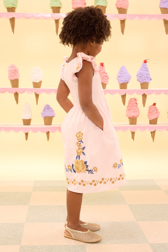 Young girl in a pink dress with floral embroidery standing in front of an ice cream cone display.
