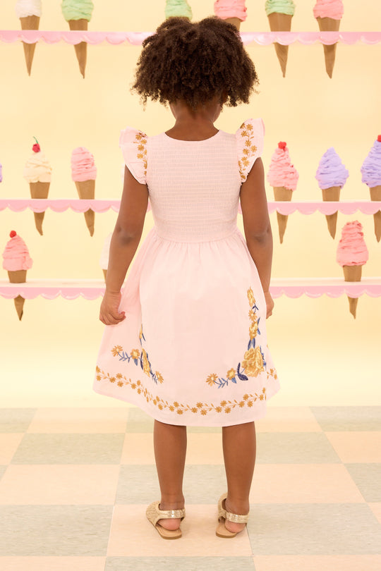 Child wearing a pink dress with floral embroidery standing in front of an ice cream cone display.