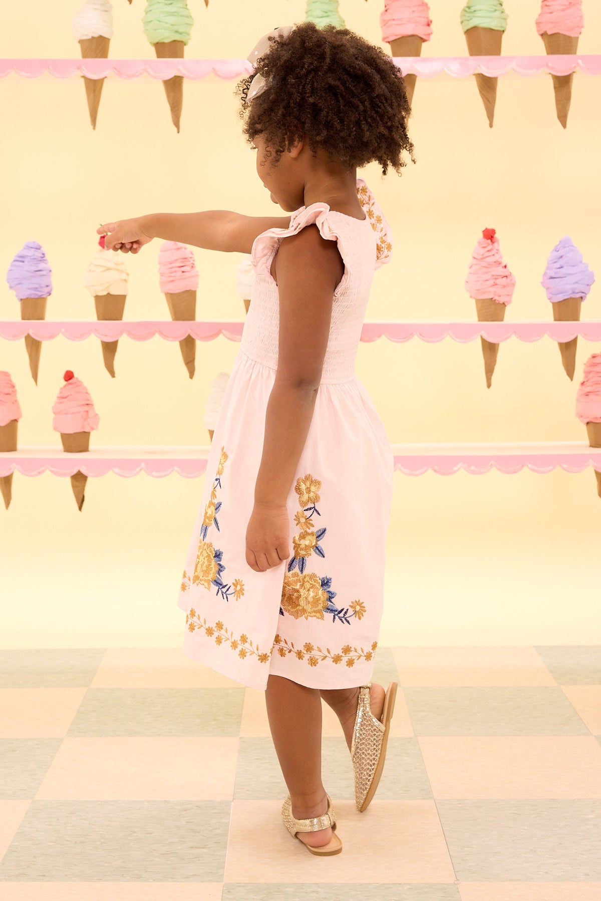 Child in a pink floral dress standing in front of an ice cream cone pattern.