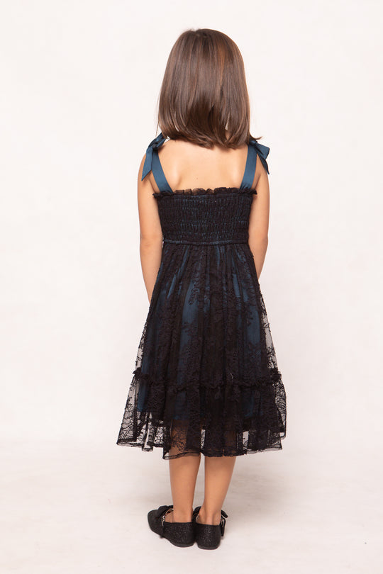 Young girl wearing a black lace dress with blue straps on a white background