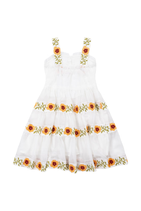 The Mini Katerina Dress by Ivy City Co is a white cotton voile dress with shoulder straps, featuring yellow and red floral embroidery with green leaves on the straps and skirt.