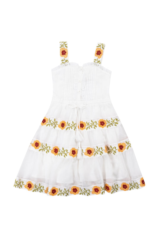 The Ivy City Co Mini Katerina Dress in White with Floral Trim is a sleeveless cotton voile dress with wide straps, red and yellow floral embroidery with green leaves on the skirt and straps, and a waist front tie.
