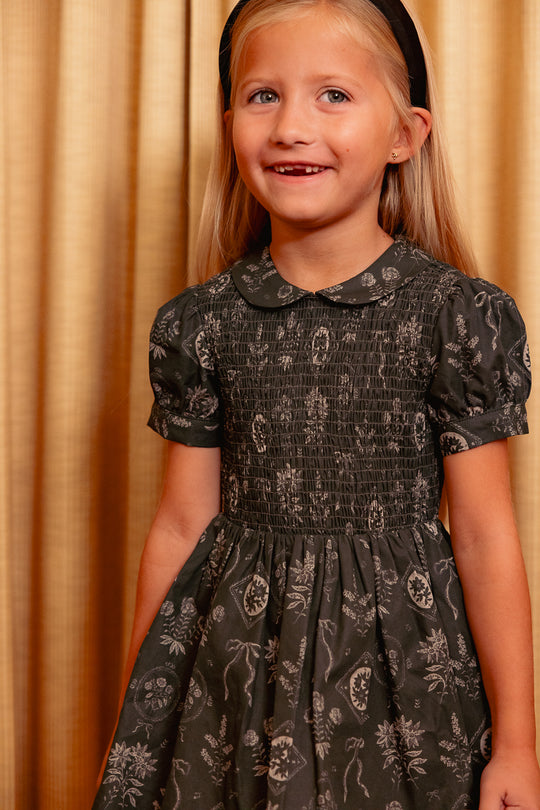 close up of a little girl in a green dress standing against a yellow curtain